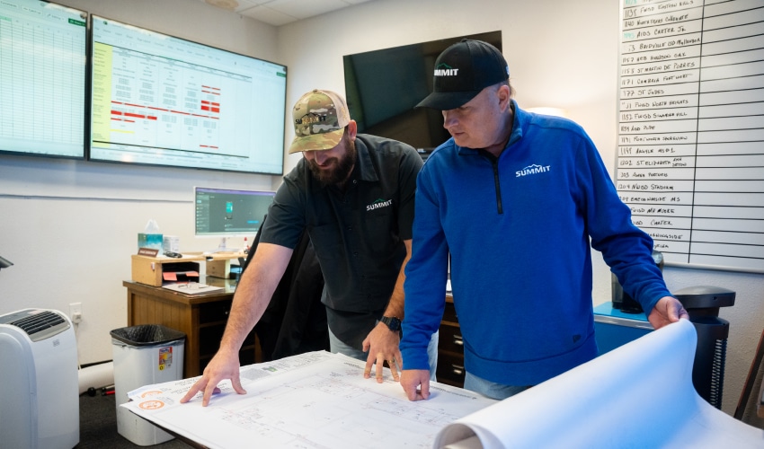 Two professionals wearing Summit Fire Consulting branded apparel reviewing architectural blueprints in an office.