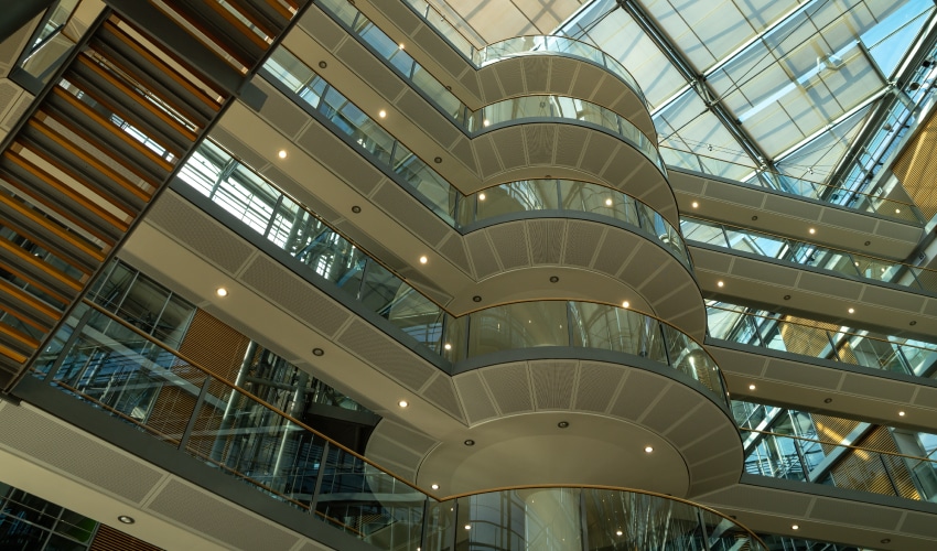A view looking up into a modern, multi-story building atrium with glass railings and curved architectural elements.