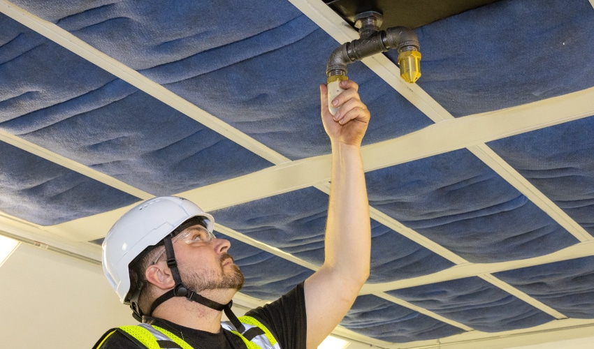 A fire safety technician inspecting a fire suppression sprinkler head on a ceiling.