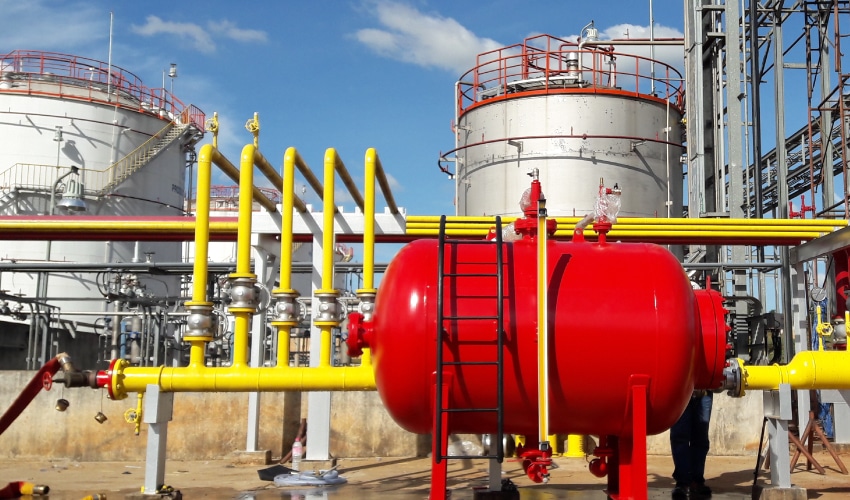 Industrial hazardous materials storage site featuring a large red tank and yellow piping network